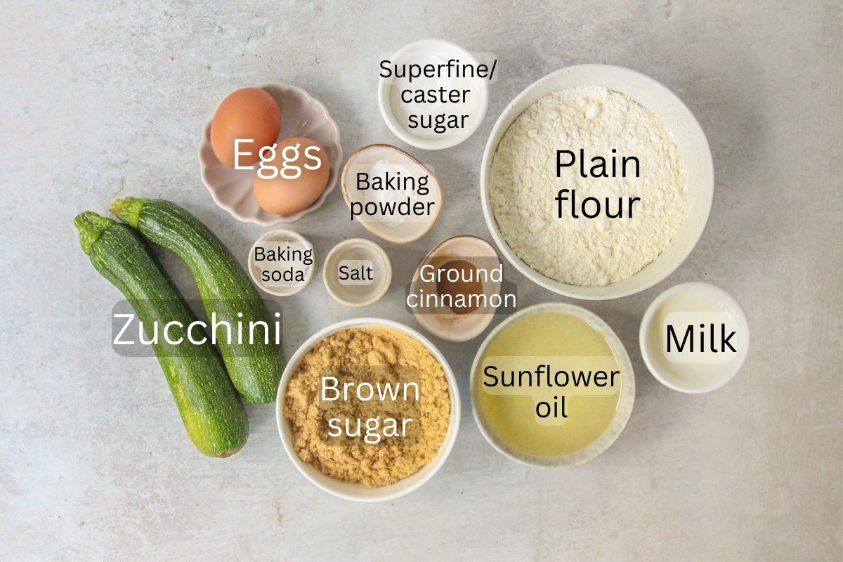 Ingredients for Zucchini Loaf Cake sit in a series of bowls on a gray surface.