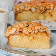 A slice of Swedish Almond Cake sits on a ceramic plate on a light gray surface.