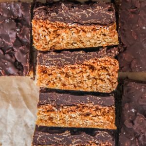 Anzac biscuit bars lay stacked on top of each other on a brown parchment paper.