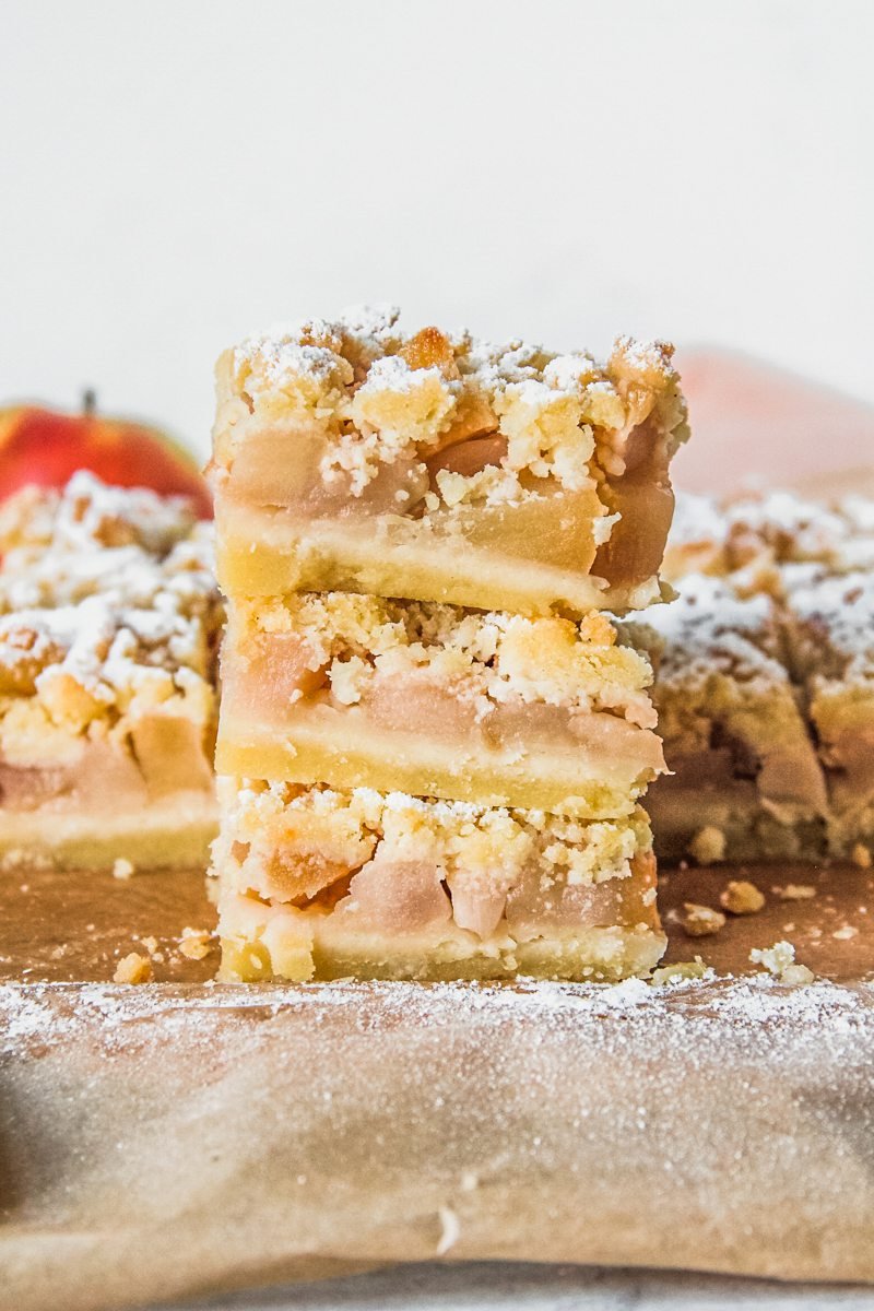 Shortbread apple bars sit stacked on parchment paper.