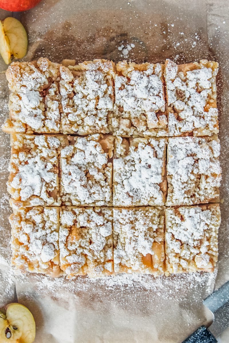 Sliced apple streusel bars sit on brown parchment paper with apple slices on the side.