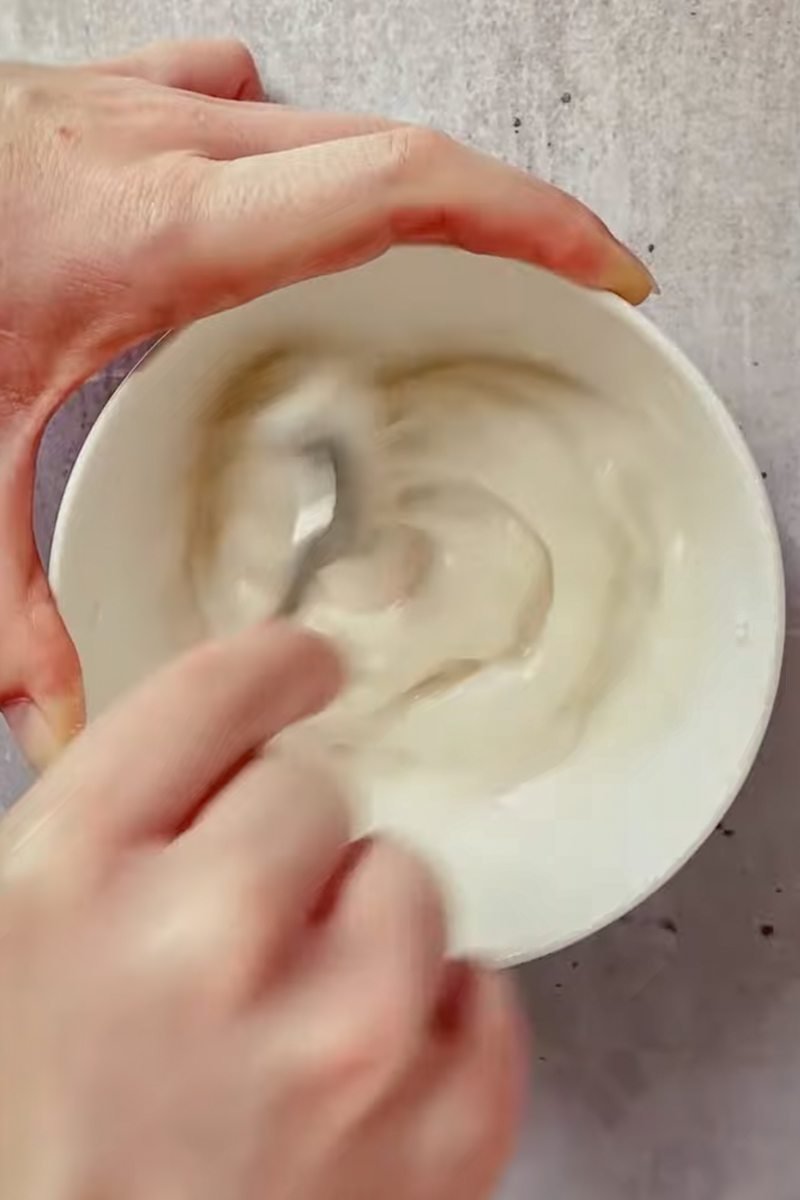 A glaze is mixed in a white ceramic bowl on a light gray surface.