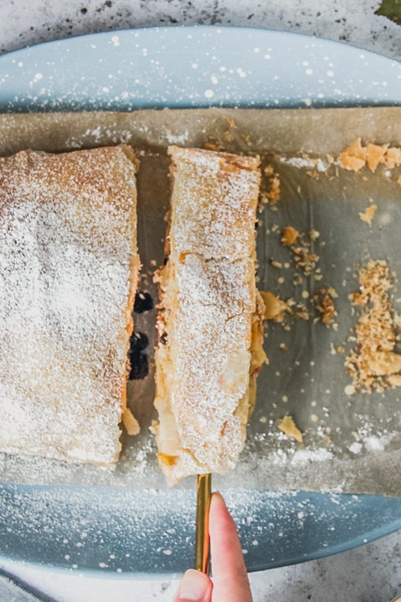 A slice of apple strudel is picked up with a serving knife.