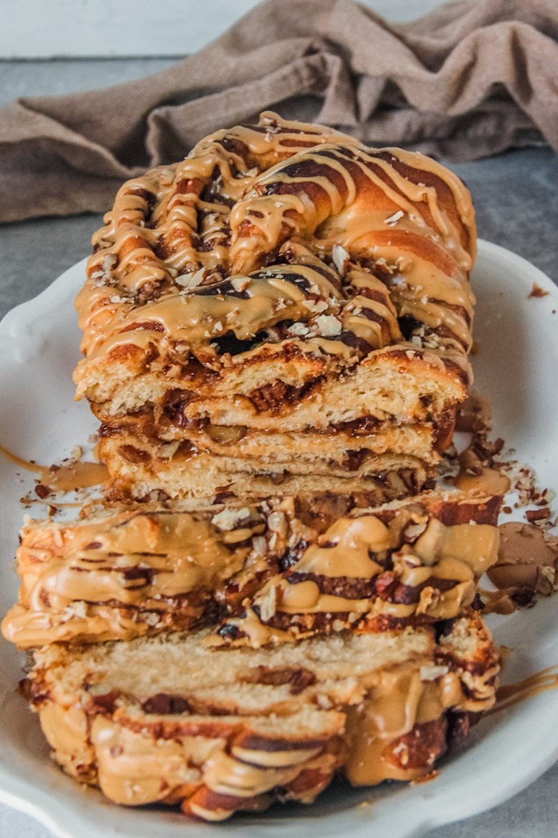 A sweet potato babka loaf with coffee glaze sits on a white oval plate on a gray surface.