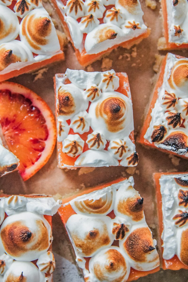 Rectangles of blood orange meringue bars sit on a parchment paper surface.