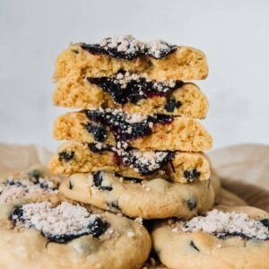 A stack of blueberry muffin cookies sit on a stack of gray plates with the blueberry jam center and light streusel on top.
