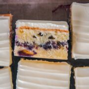 A slice of blueberry sheet cake sits on it's side with the line of homemade blueberry streusel center and layer of cream cheese frosting visible.