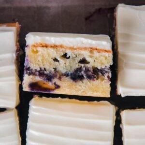 A slice of blueberry sheet cake with a line of homemade blueberry streusel in the center and a thin layer of cream cheese frosting on top.