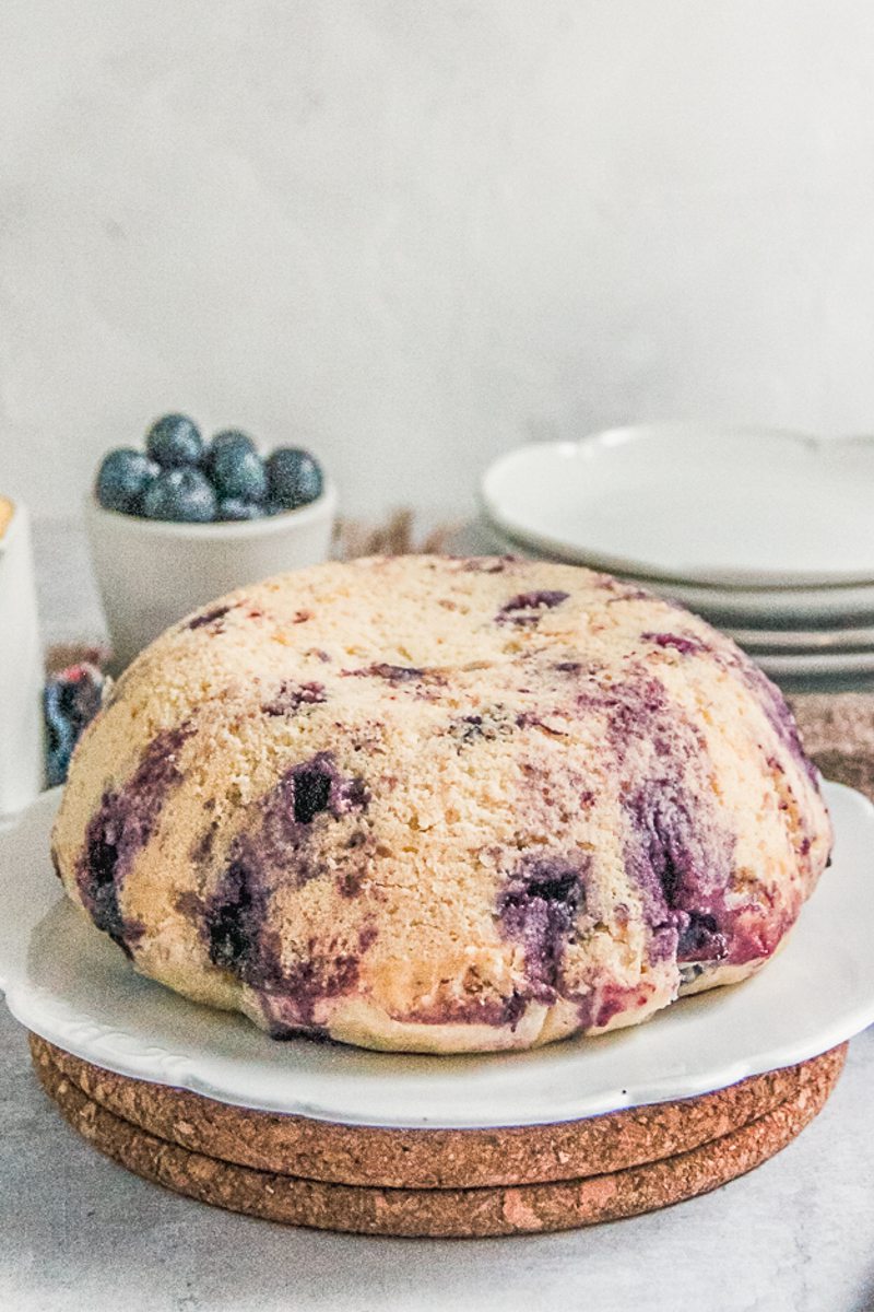 Steamed blueberry pudding sits on a white ceramic plate on two cork mats on a gray surface.