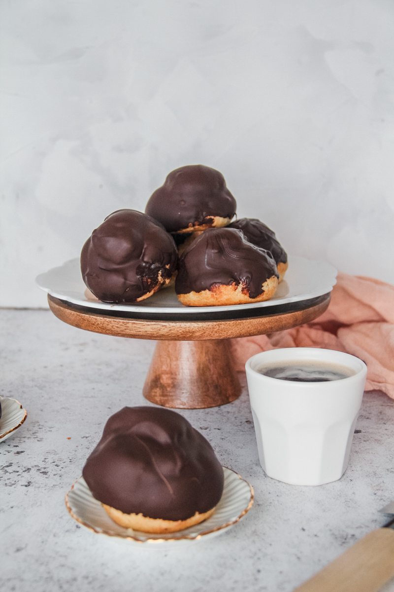 Dutch profiteroles sit on an individual plate and cake stand on a light gray surface.