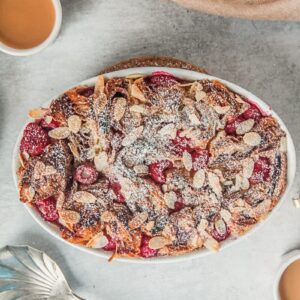 Croissant bread pudding in an oval white baking dish sits on a gray surface.