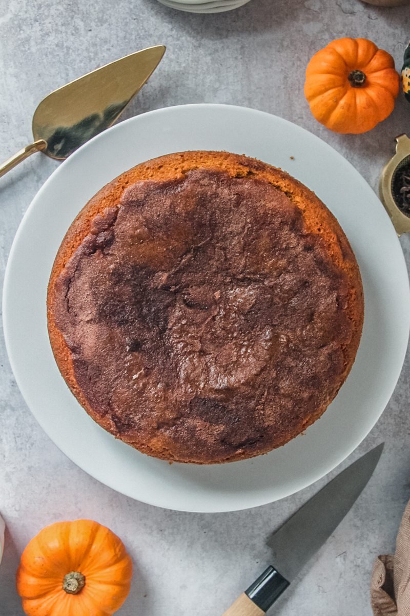 A browned butter pumpkin cake sits served up on a white plate on a gray surface.