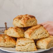 Buttermilk biscuits sit stacked up on a white plate on a gray surface.