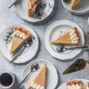 Slices of butterscotch pie sit on white ceramic plates on a gray surface with a cup of coffee beside.