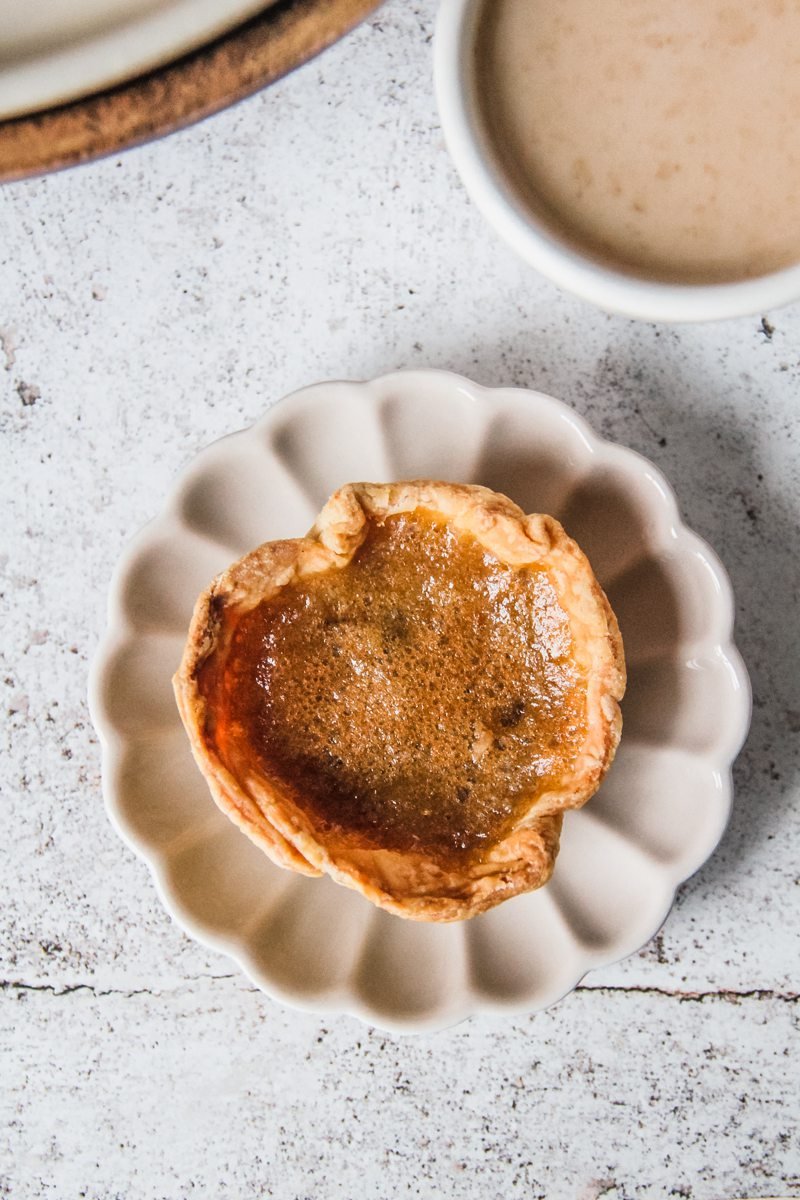 A single golden butter tart sits on an individual plate on a light gray surface.