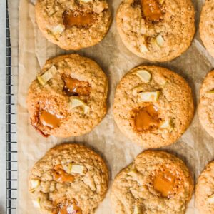 Apple caramel cookies sit on a cooling rack lined with greaseproof paper on a gray surface.