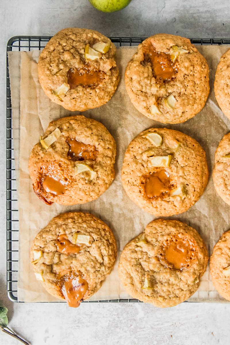 Apple caramel cookies sit on a cooling rack lined with greaseproof paper on a gray surface.