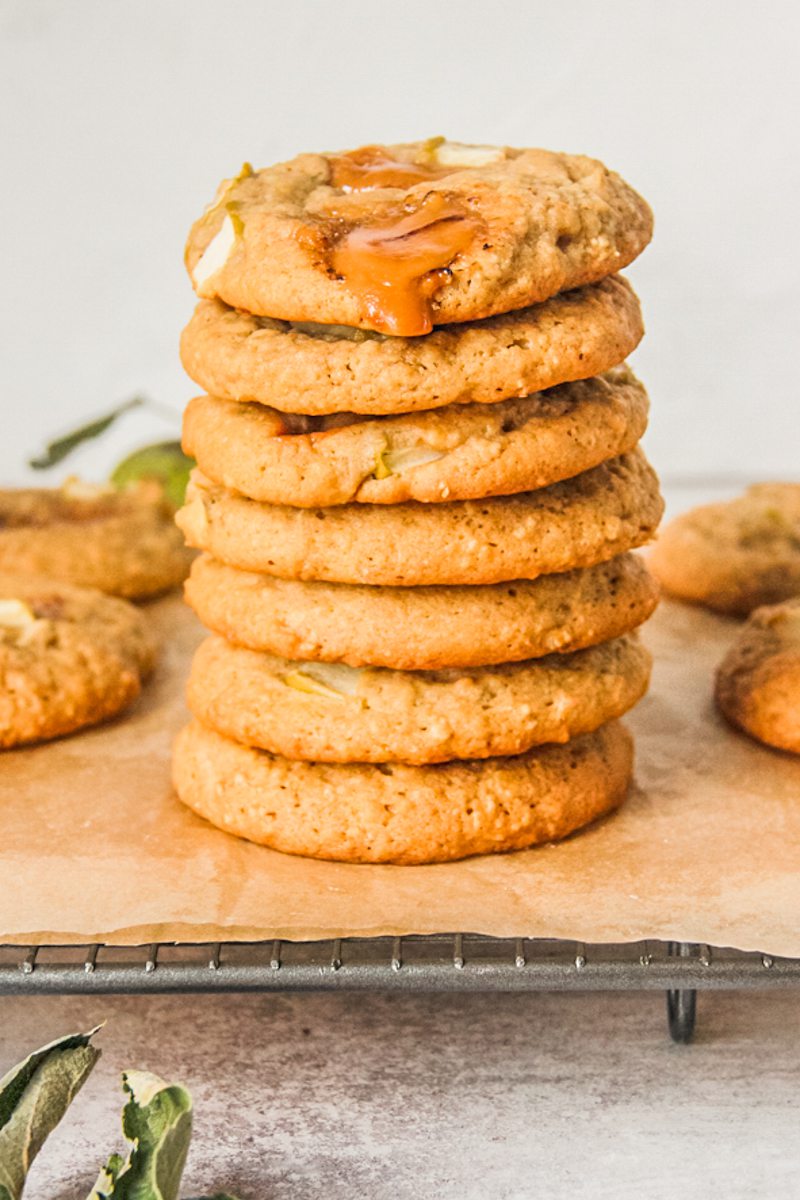 A stack of apple caramel cookies sit on a cooling rack lined with greaseproof paper on a gray surface.