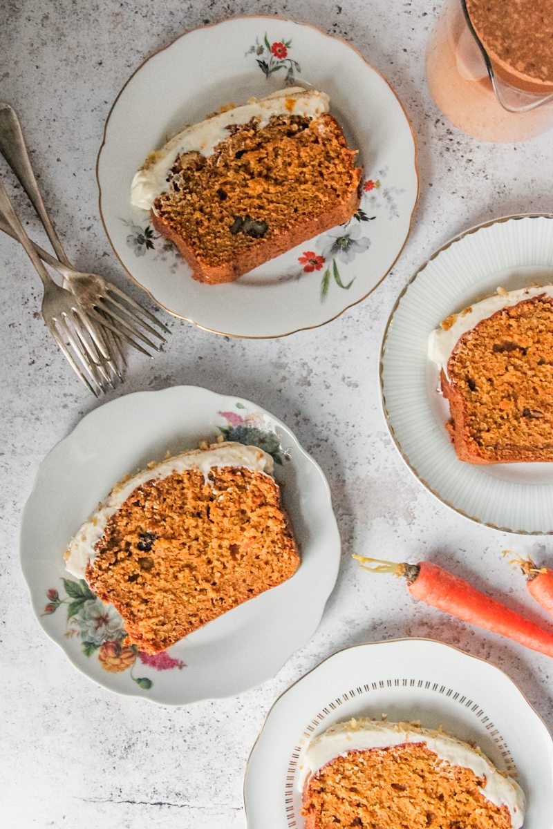 Slices of carrot cake loaf sit on individual plates on a light gray surface.