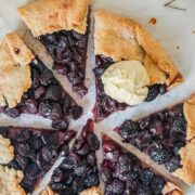 Slices of cherry galette sit on parchment paper on a light gray surface with one scoop resting on a slice of galette.