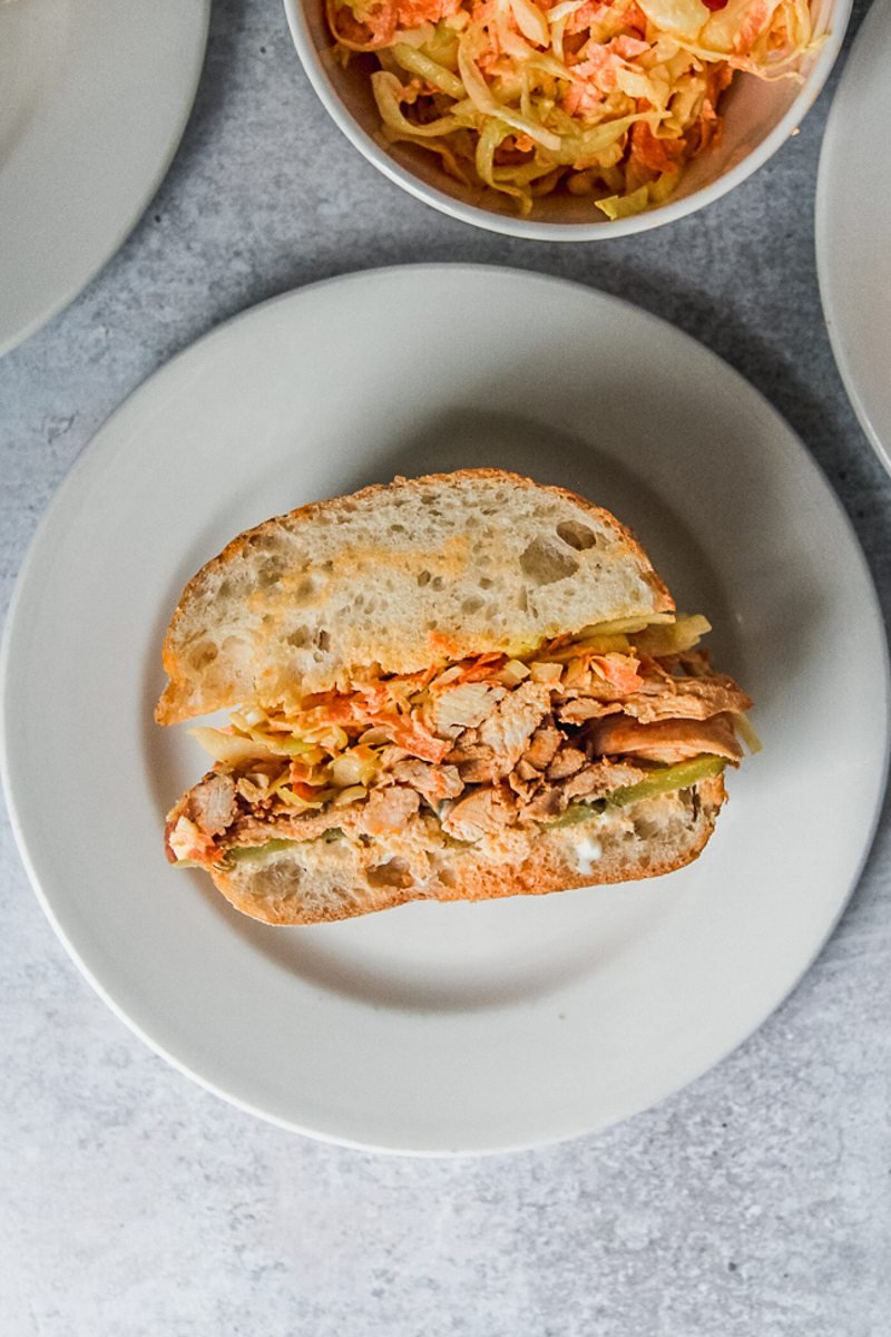 A spiced chicken sandwich sits on a white ceramic plat on a gray surface.