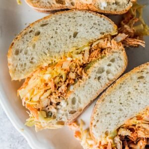 A side on view of shredded spiced chicken and coleslaw in thick bread sits on an oval white ceramic plate on a gray surface.