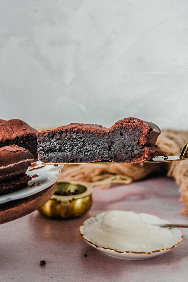 A slice of French chocolate cake sits on a cake server with it's fudgy center visible above a light pink background.