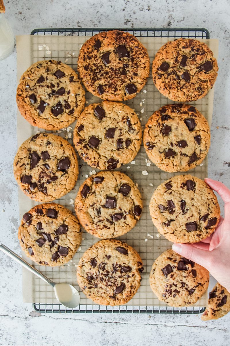 Tahini oatmeal chocolate chunk cookies sit on a lined cooling rack above a light gray surface.