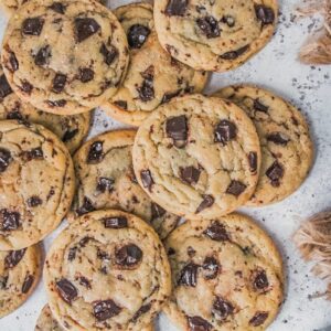 Chocolate chunk cookies lay strewn on each other on a light gray surface.