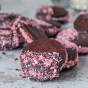 A chocolate peppermint sandwich cookie decorated with crushed candy canes rests on another cookie on a light gray surface.
