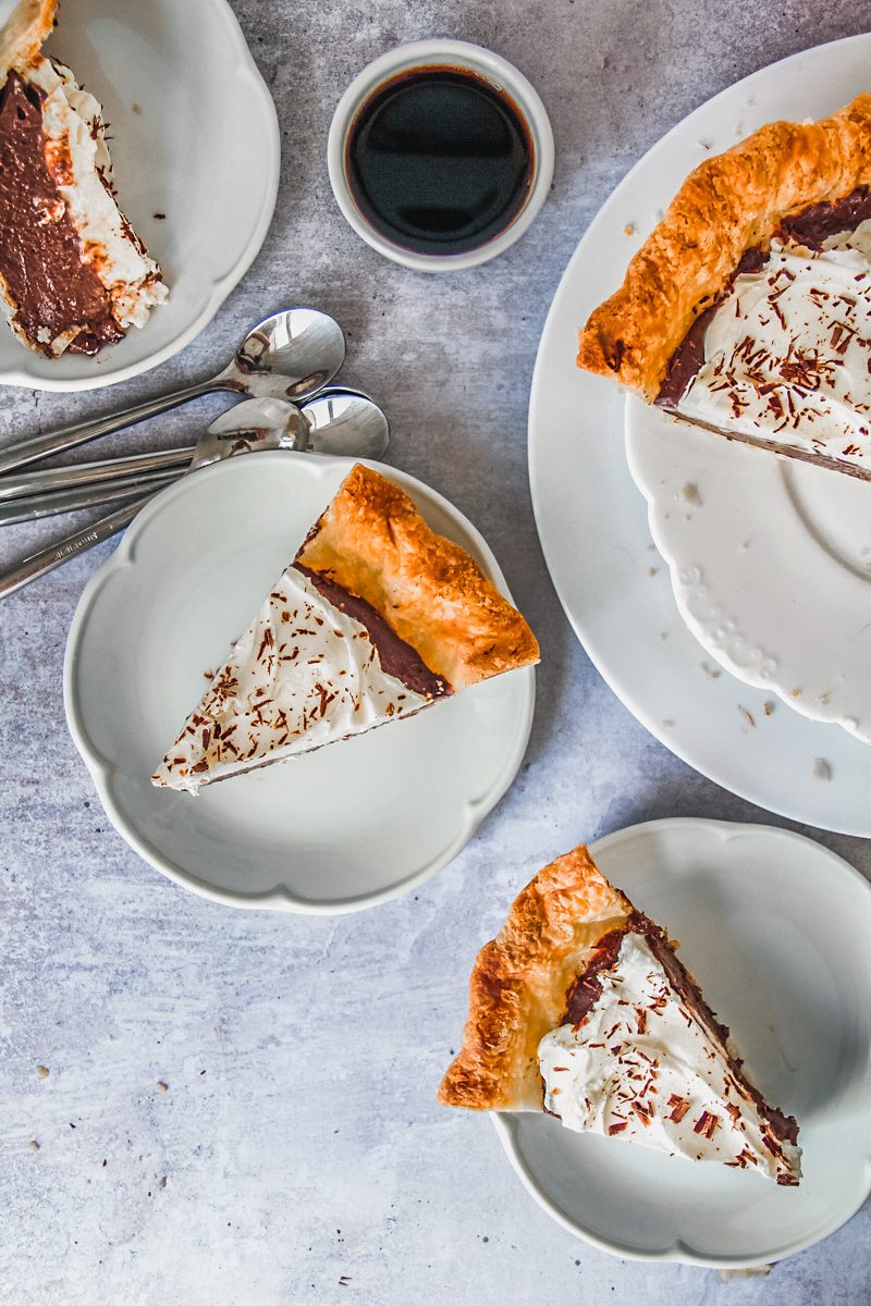 Slices of chocolate pudding pie sit on individual plates on a gray surface.