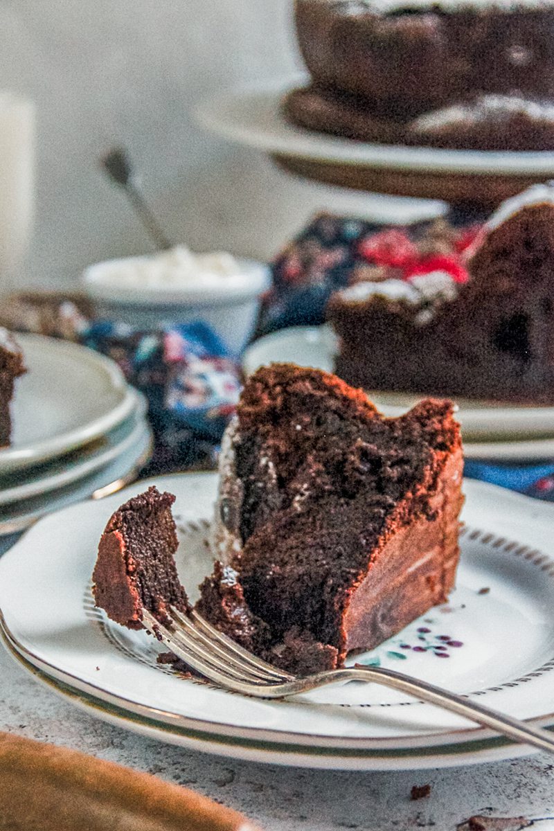 A slice of flourless chocolate cake sits on two ceramic plates with a portion on a fork resting on the plate on a light gray surface.