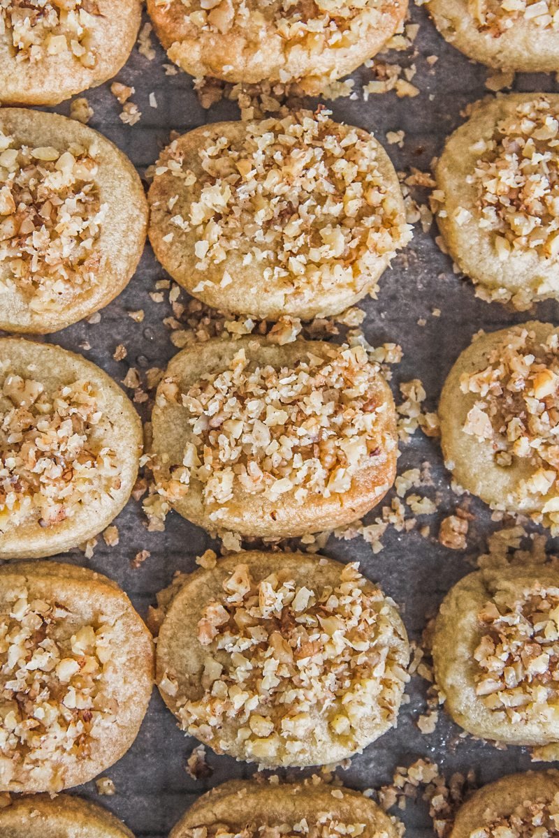 Greek christmas cookies sit on parchment paper on a cooling rack.