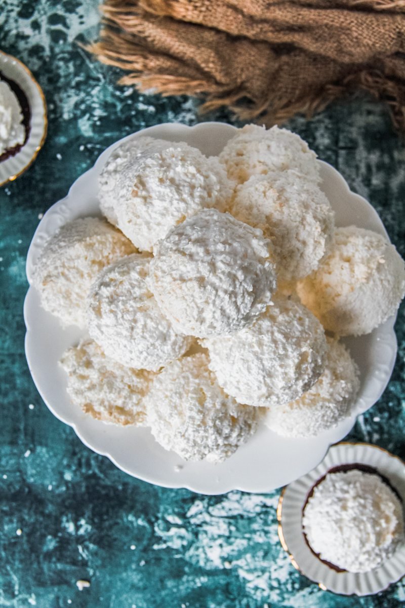 Austrian coconut meringue cookies sit on a white fluted ceramic plate above a green and white surface.