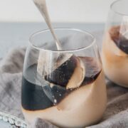 A spoonful of panna cotta rests on the remaining dessert in a glass on a gray cloth on a blue gray surface.