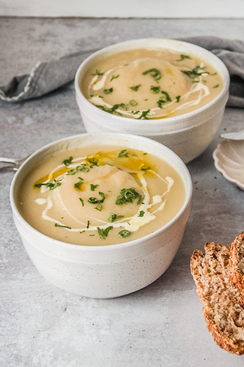 Individual servings of Irish Potato soup sit in white round ceramic bowls beside a bowl of rice on a gray surface.