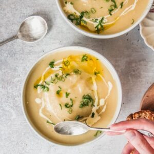 Individual portions of Colcannon soup sit in white round ceramic bowls beside a bowl of rice on a gray surface.