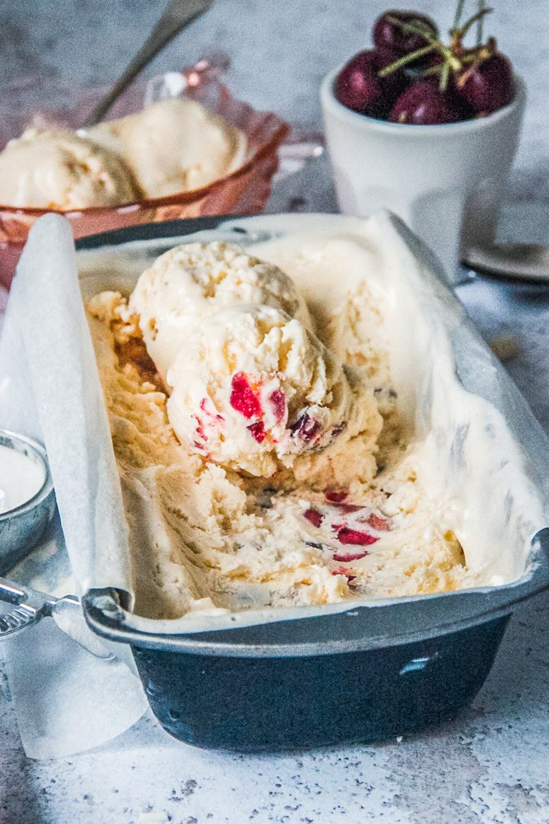 Scoops of white chocolate cherry semifreddo sit on top of a lined metal rectangle tray on a light gray surface.