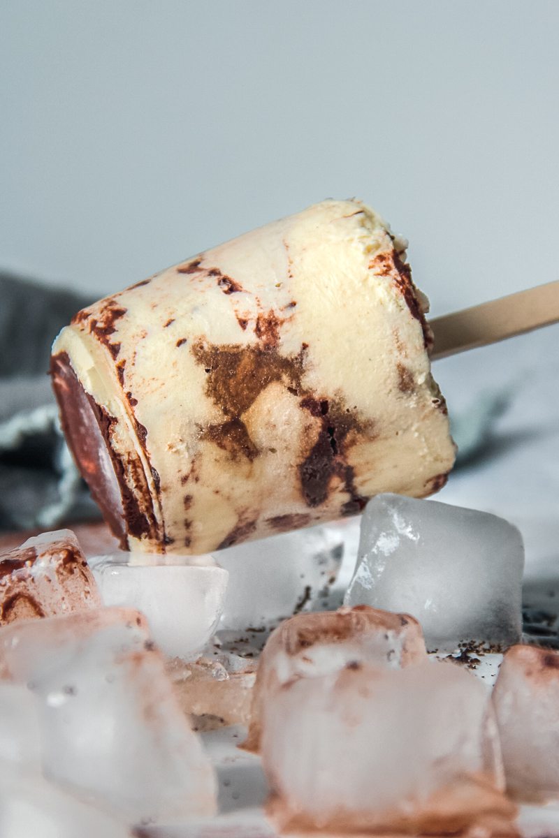 Frozen tiramisu rests on ice cubes with it's custard layers visible.