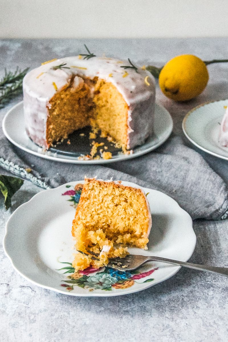 A slice of dairy free lemon cake sits on a fluted ceramic plate with a portion of the front of the slice resting on a fork.