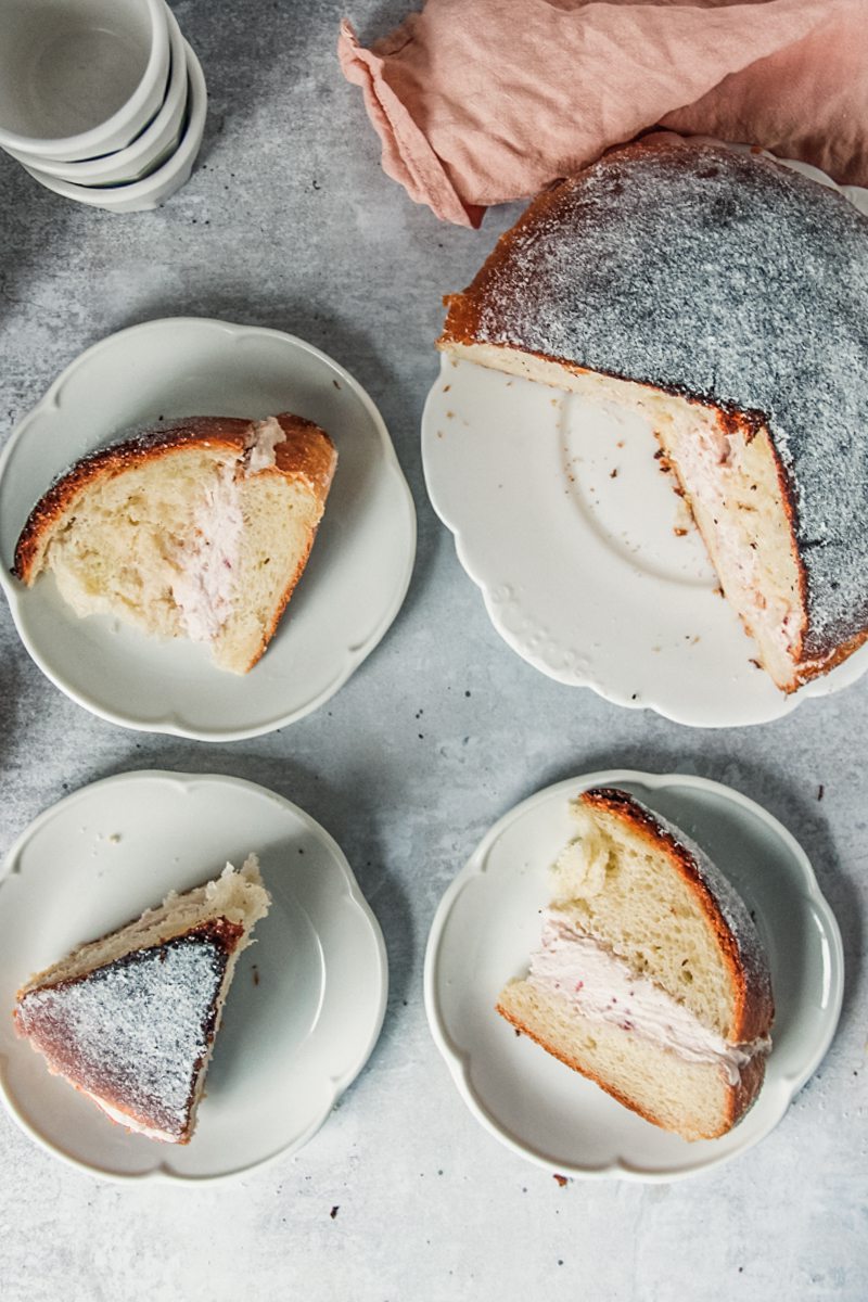 Slices of Sufganiyot or Donut cake sit served up on individual white ceramic plates with the jam cream filling visible on a gray surface.