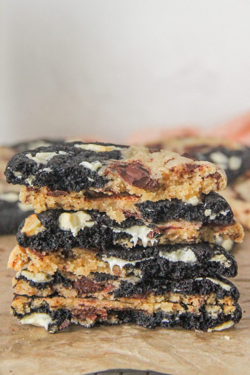 Triple chocolate cookies sit halve and stack on each other with the two sides visible and melting chocolate sits on brown paper.