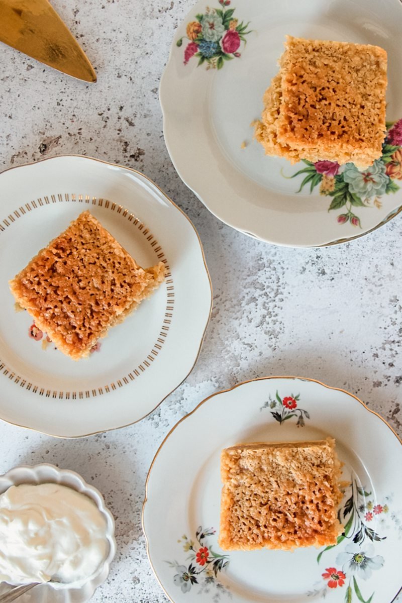 Square slices of Danish dream sit served up on individual plates on a gray surface served beside a small plate of Greek yogurt.