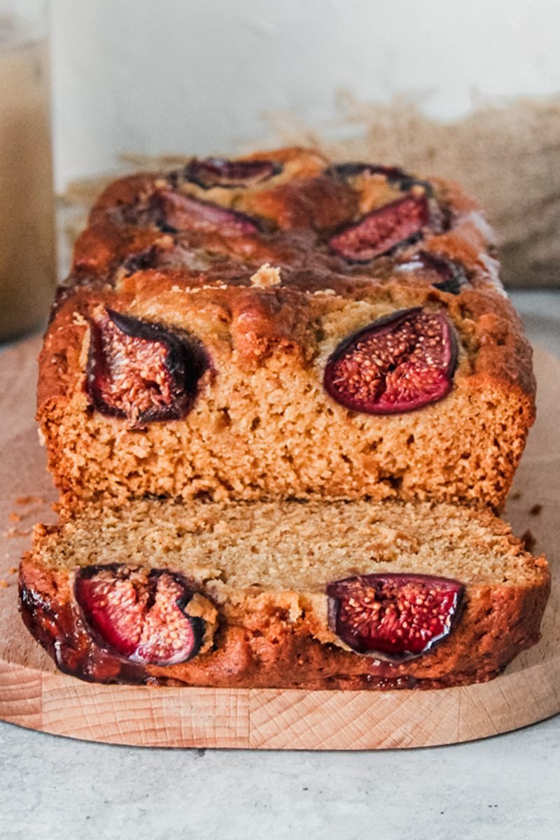 A slice of fig loaf cake sits on it's side with the warm brown interior visible on a wooden board on a gray surface.