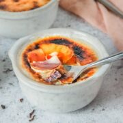 A spoonful of custard is heaped up from a gray ceramic ramekin on a light gray surface.