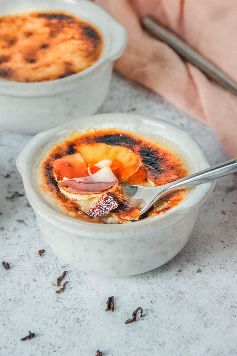 A spoonful of custard is heaped up from a gray ceramic ramekin on a light gray surface.