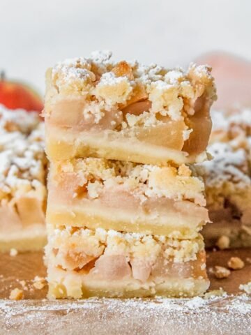 Shortbread apple bars sit stacked on parchment paper with the remaining bars sitting behind.