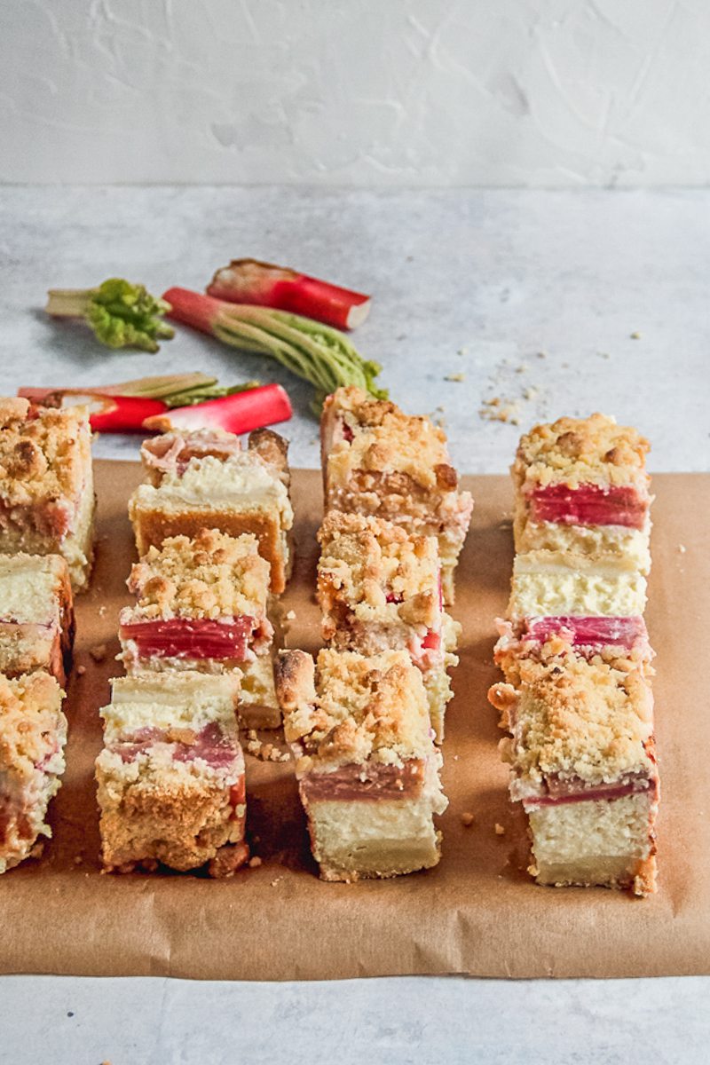 Squares of Estonian Rhubarb Cheesecake sit on parchment paper on a gray surface.