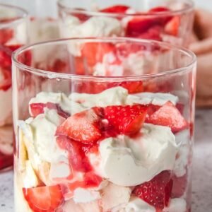 An individual serving of Eton Mess sits in a glass on a light grey background.