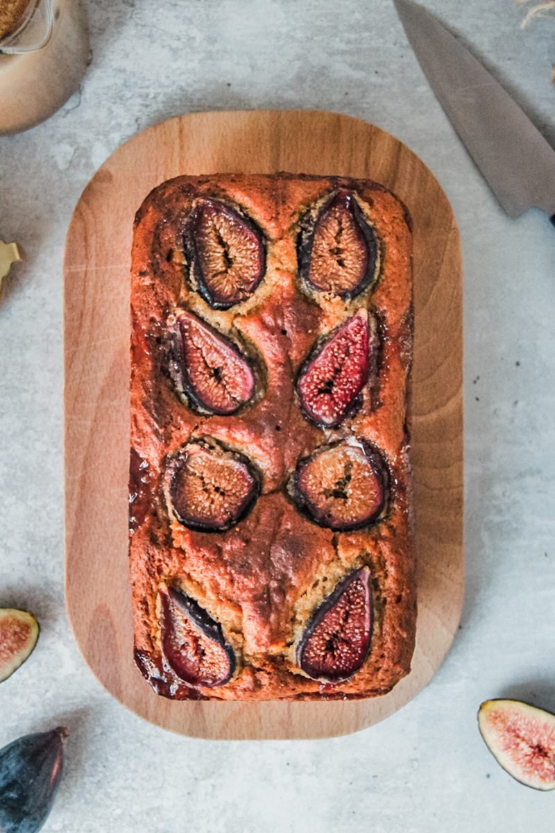 Fig loaf cake with baked fresh figs on top sits on an oval wooden board on a gray surface.